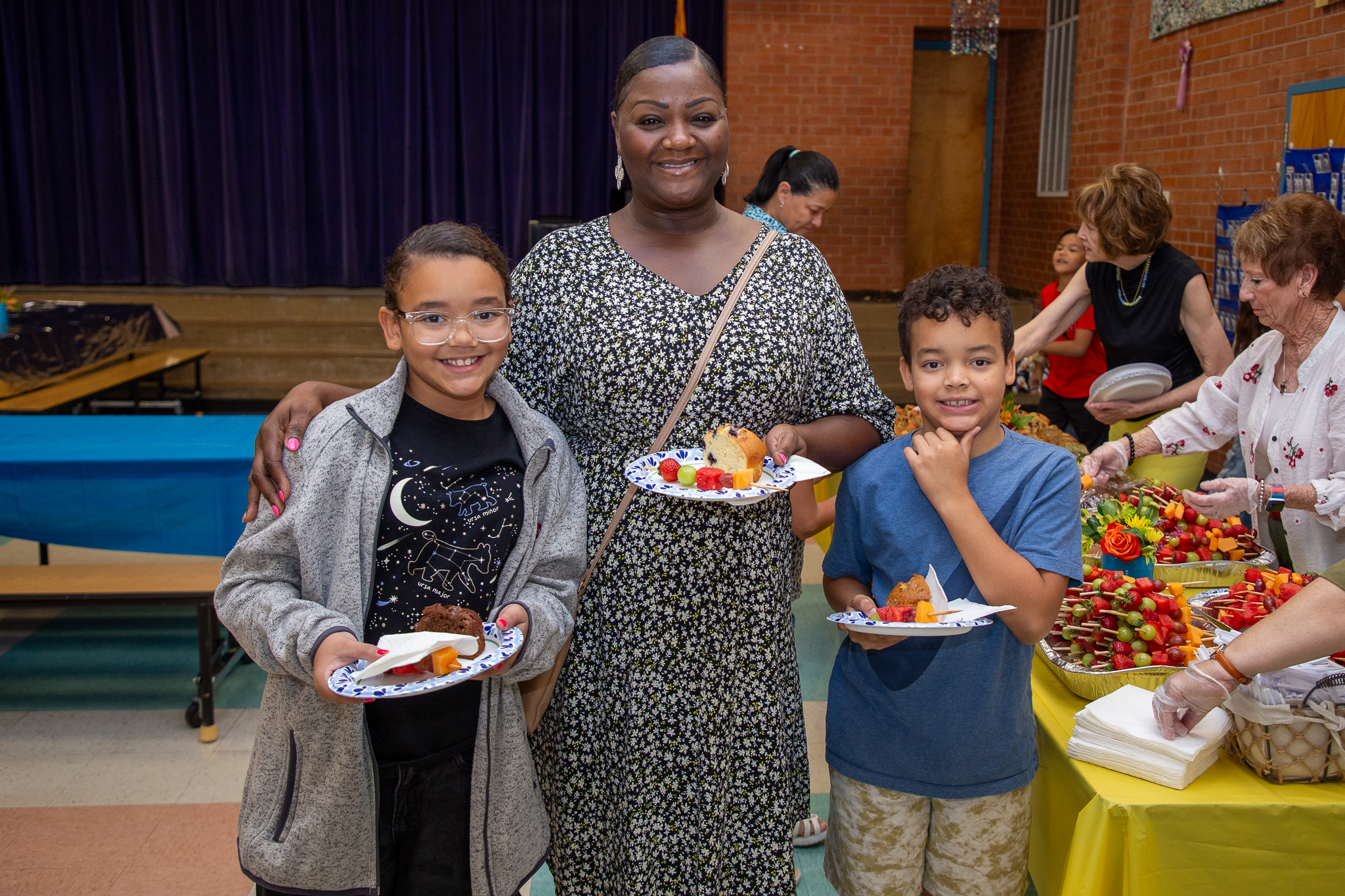 A grandma smiles with her granddaughter and grandson holding their breakfast treats