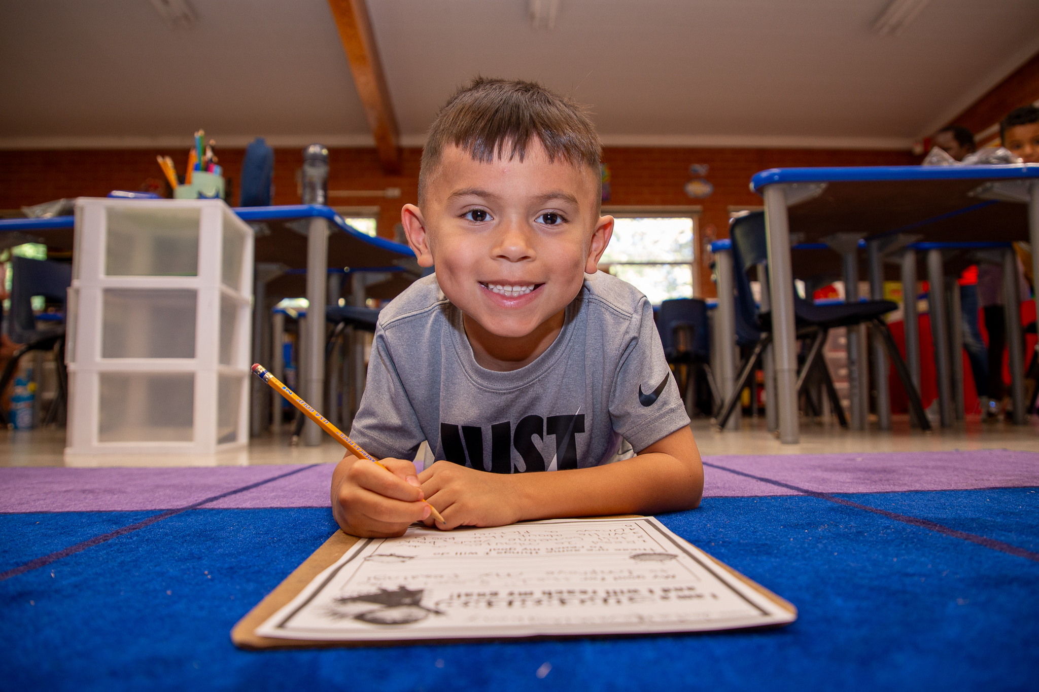 A little boy smiles as he works on an assignment on the rug