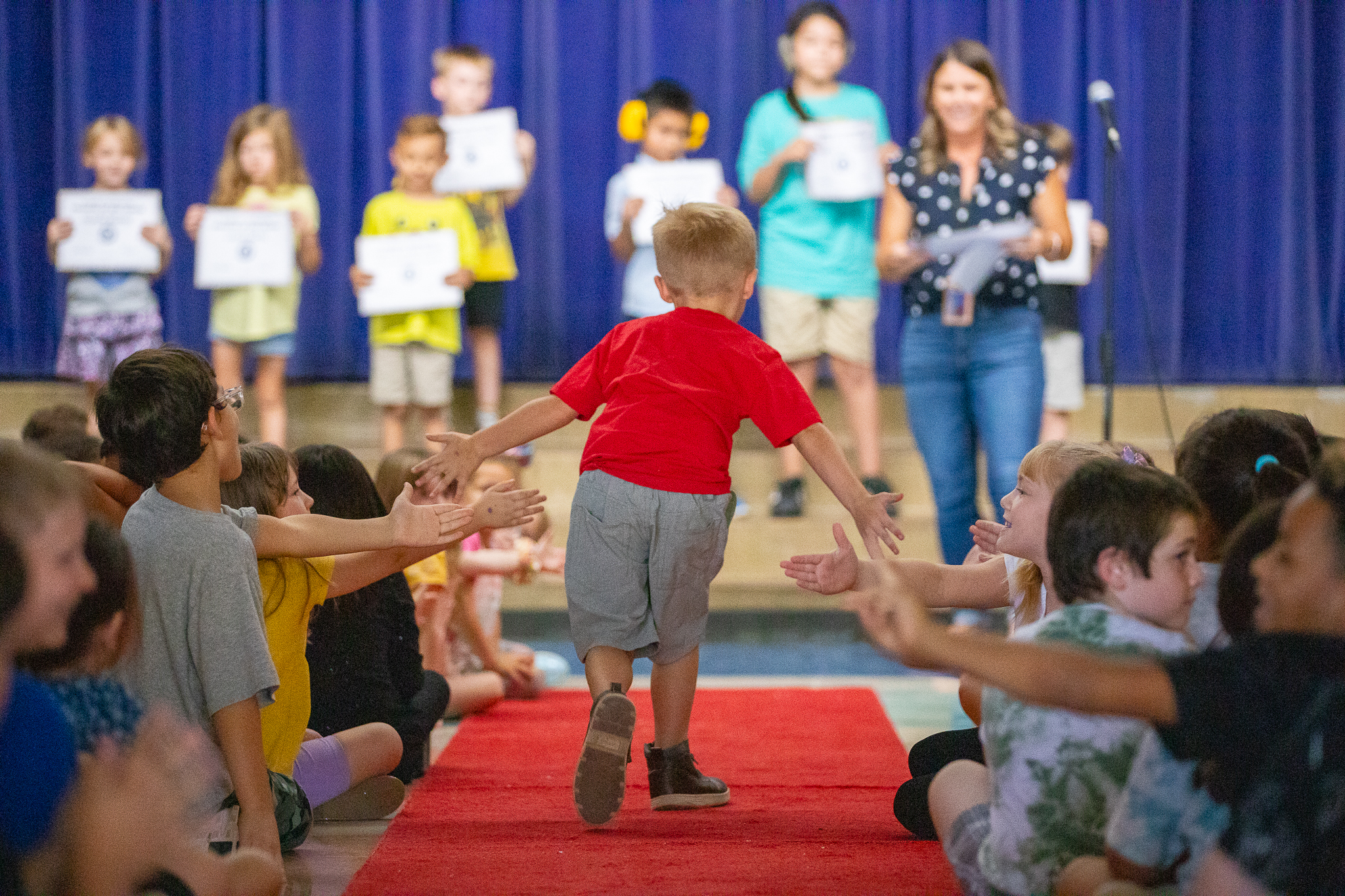 A boy gives out high fives as he walks up to the stage on a red carpet