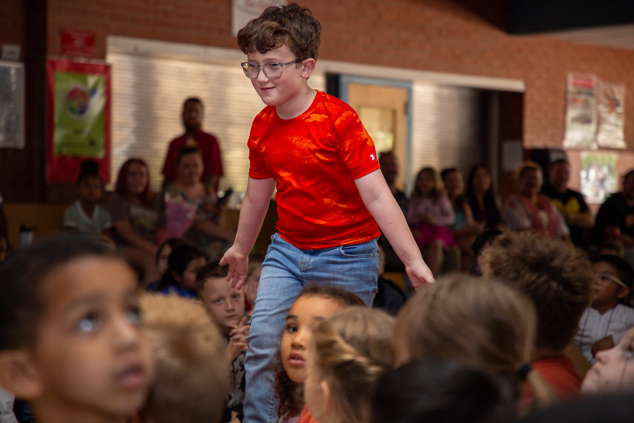 A boy in a red shirt and glasses high fives his classmates on the way up to the stage