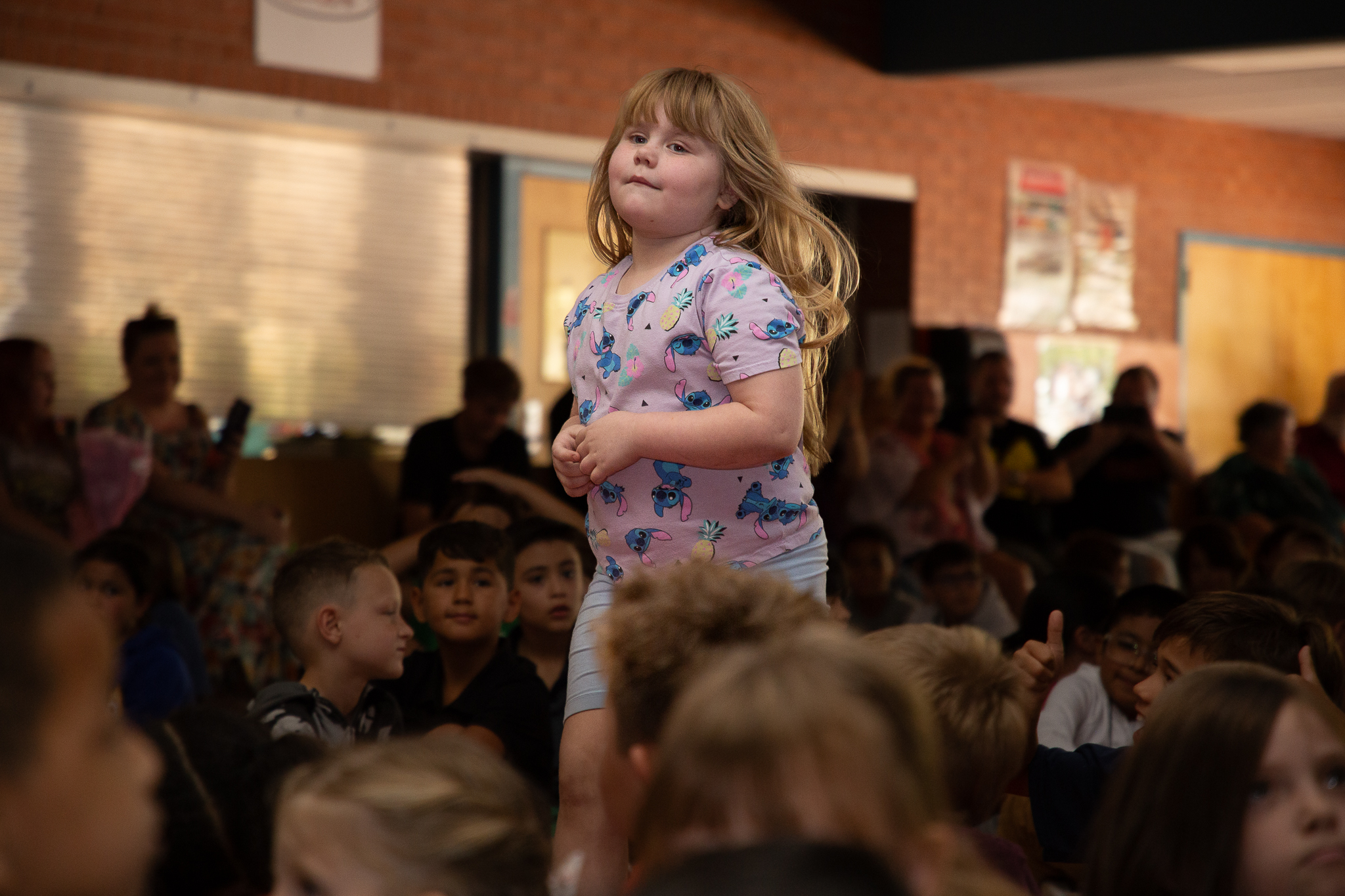 A little girl in a pink shirt runs up to the stage to get her certificate