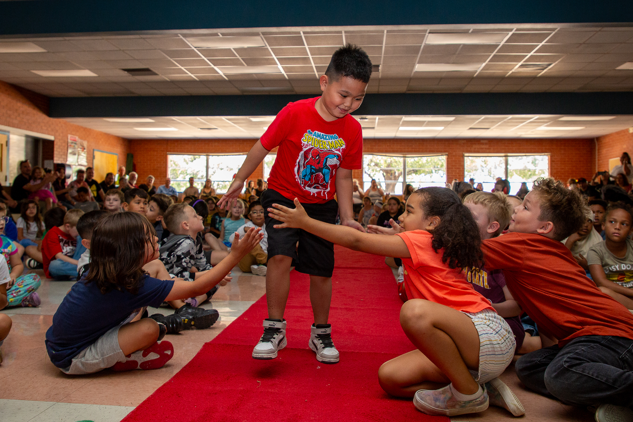 A boy in a red shirt smiles and gives out high fives on the red carpet