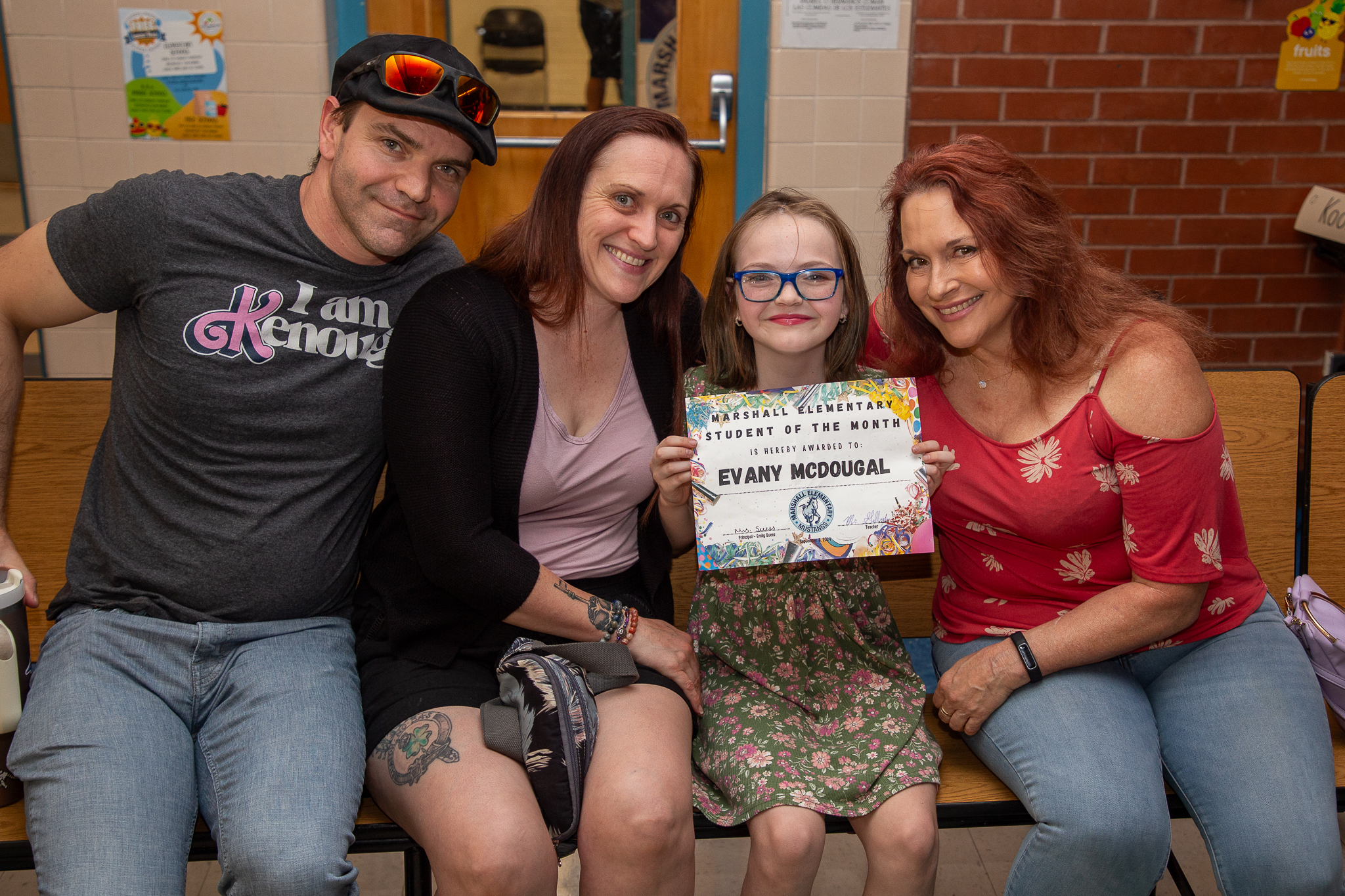 A little girl in glasses smiles with her student of the month certificate and her family smiles next to her