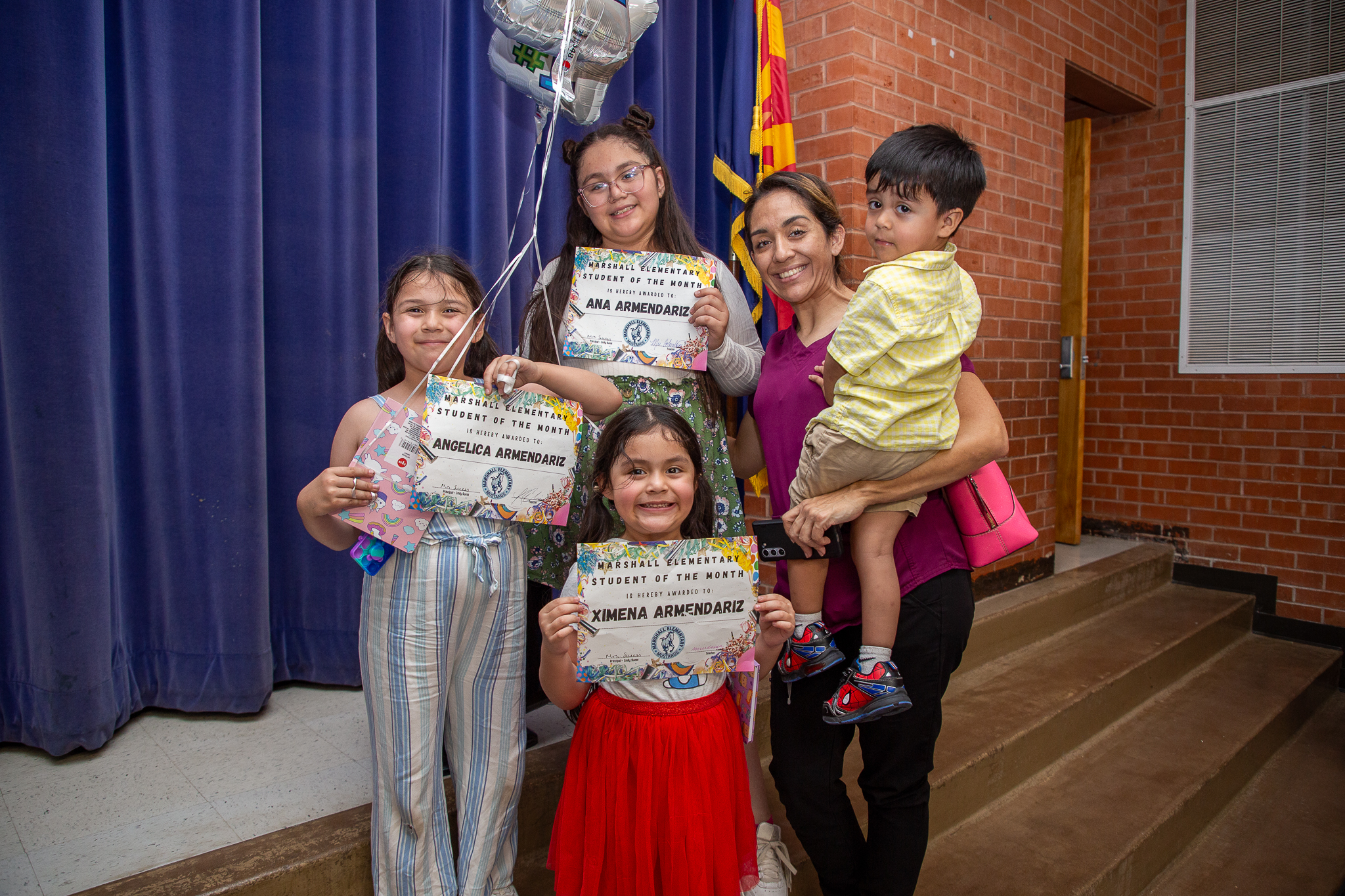 Three sisters smile with their certificates and pose with their mom and little brother