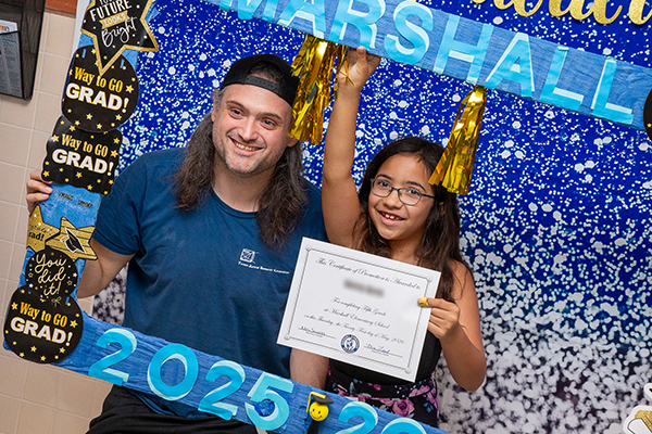 A girl poses with her promotion certificate and her dad in a graduation photo frame
