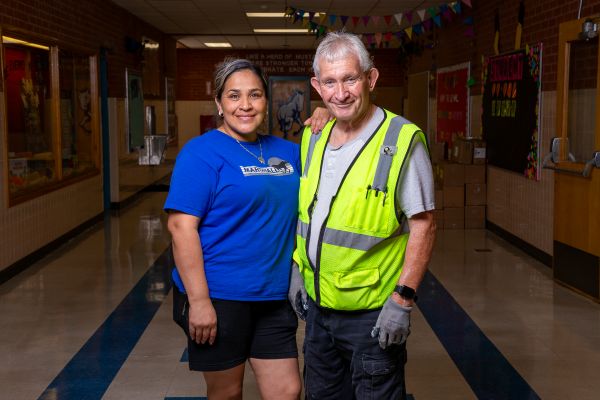 A woman and man smile in a school hallway