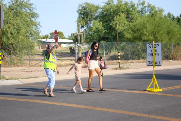 A crossing guard escorts a mom and daughter across the street