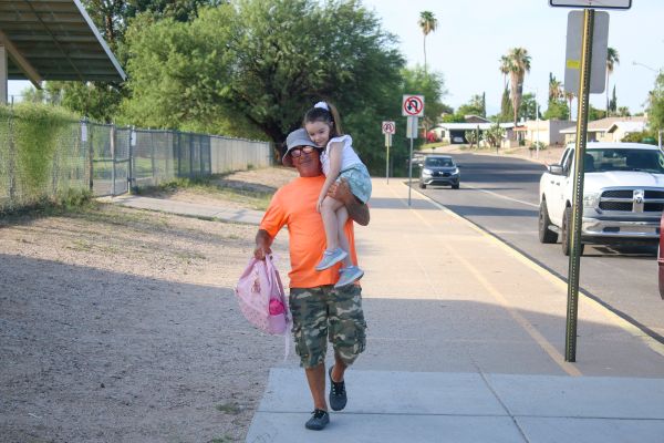 A dad carries his daughter into the school courtyard